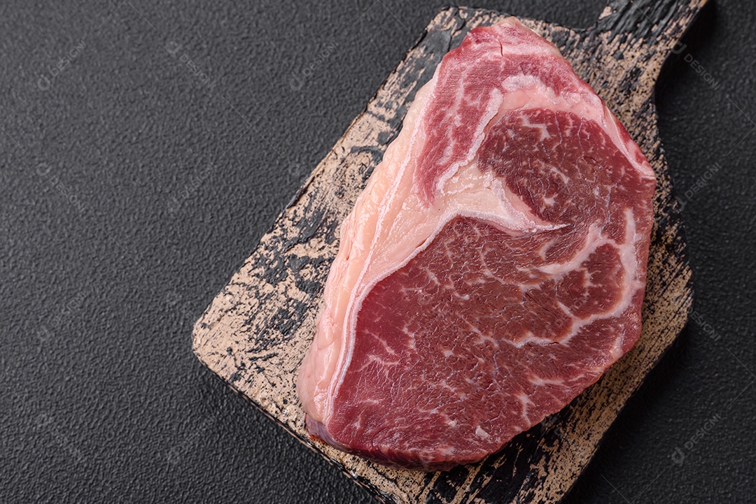 Bife de carne crua fresca com sal, especiarias e ervas sobre um fundo escuro de concreto