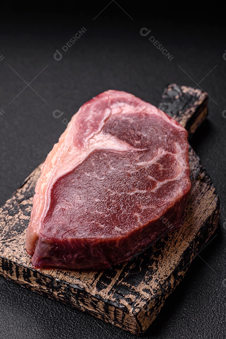 Bife de carne crua fresca com sal, especiarias e ervas sobre um fundo escuro de concreto
