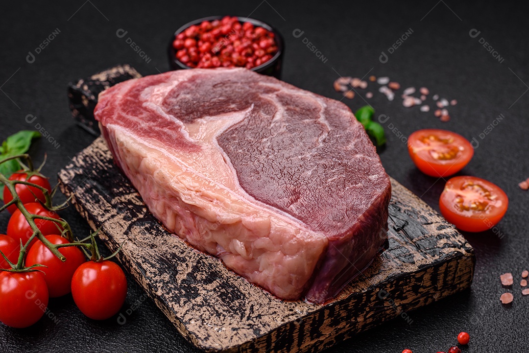 Bife de carne crua fresca com sal, especiarias e ervas sobre um fundo escuro de concreto