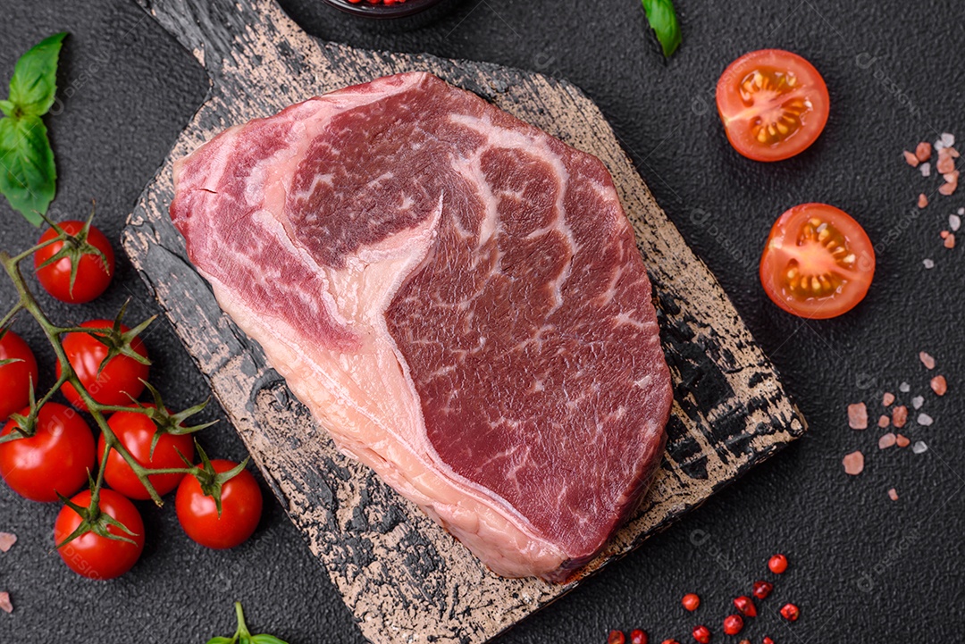 Bife de carne crua fresca com sal, especiarias e ervas sobre um fundo escuro de concreto