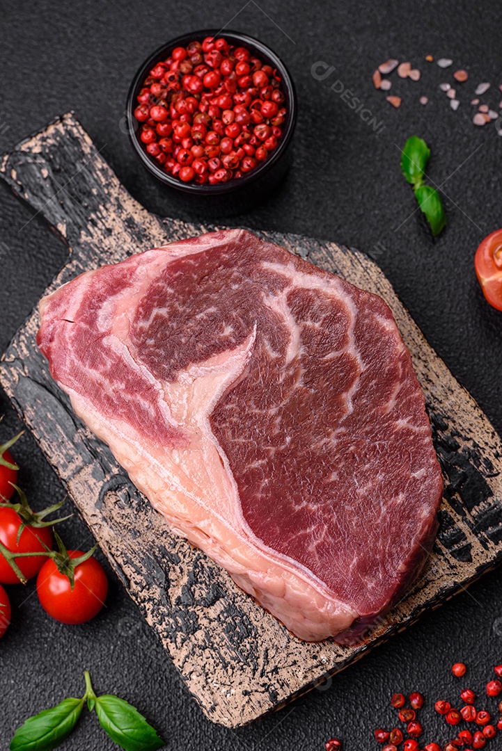 Bife de carne crua fresca com sal, especiarias e ervas sobre um fundo escuro de concreto