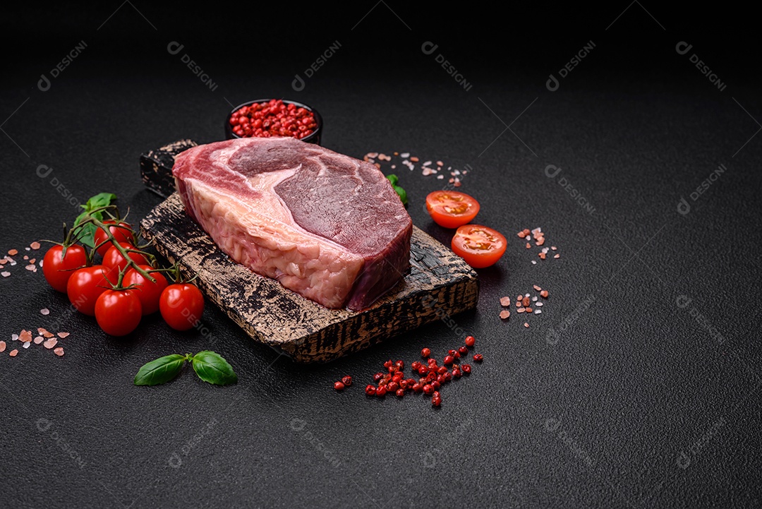 Bife de carne crua fresca com sal, especiarias e ervas sobre um fundo escuro de concreto