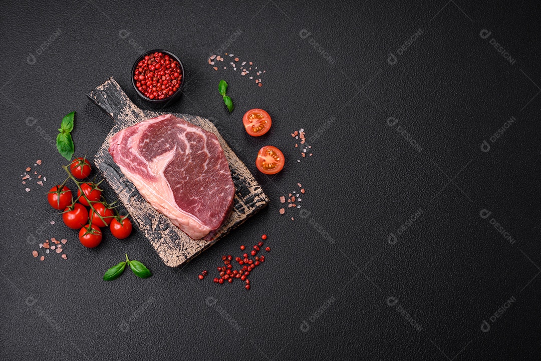Bife de carne crua fresca com sal, especiarias e ervas sobre um fundo escuro de concreto