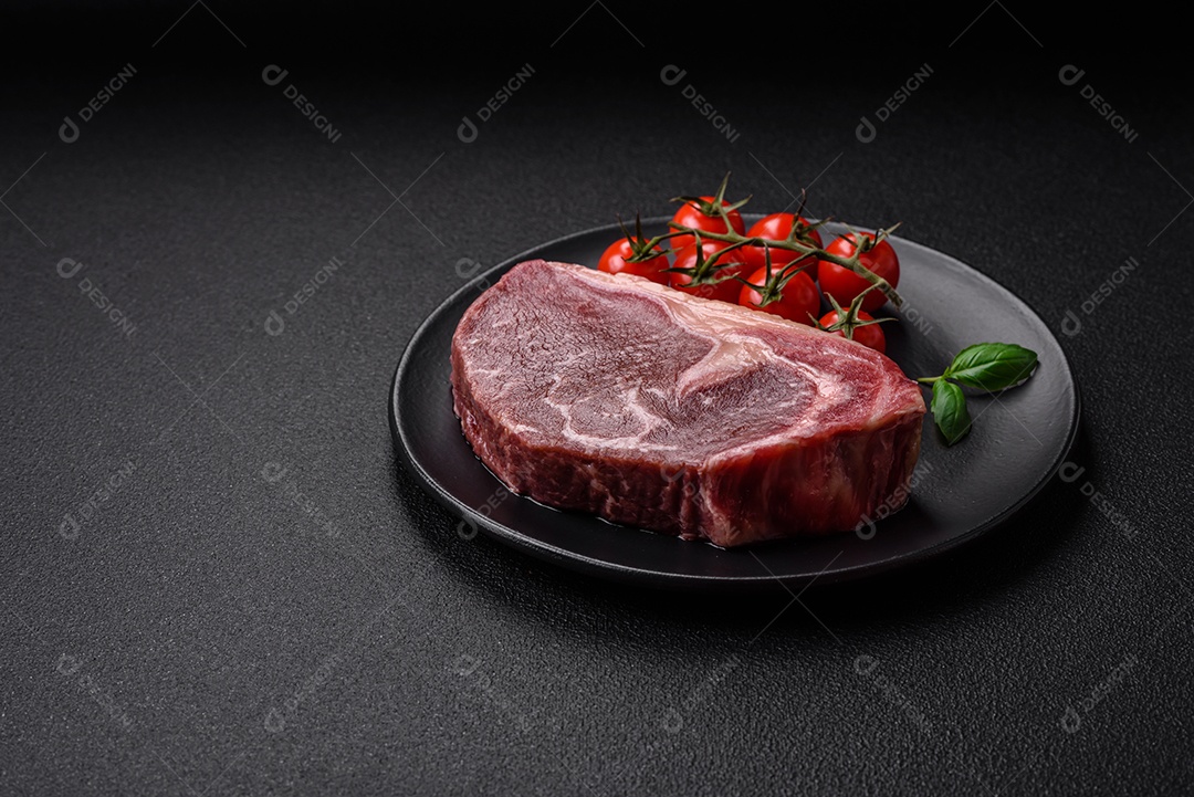 Bife de carne crua fresca com sal, especiarias e ervas sobre um fundo escuro de concreto