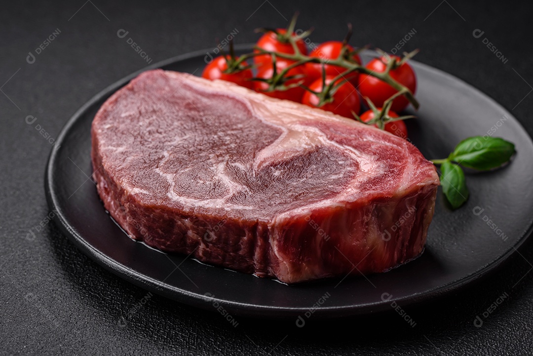 Bife de carne crua fresca com sal, especiarias e ervas sobre um fundo escuro de concreto
