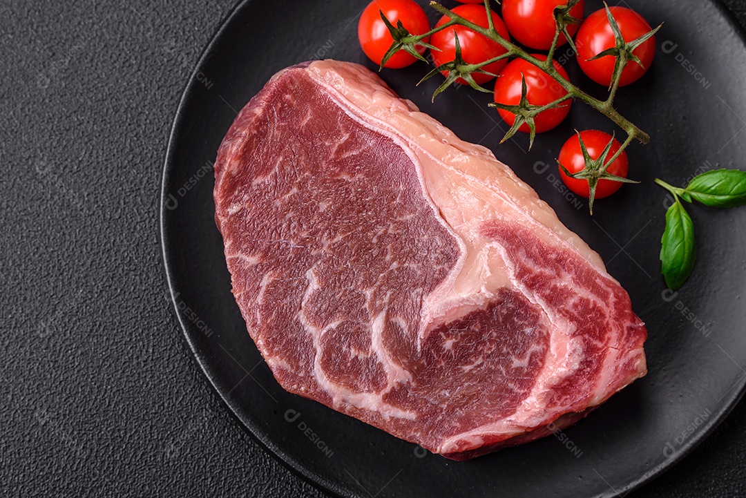 Bife de carne crua fresca com sal, especiarias e ervas sobre um fundo escuro de concreto