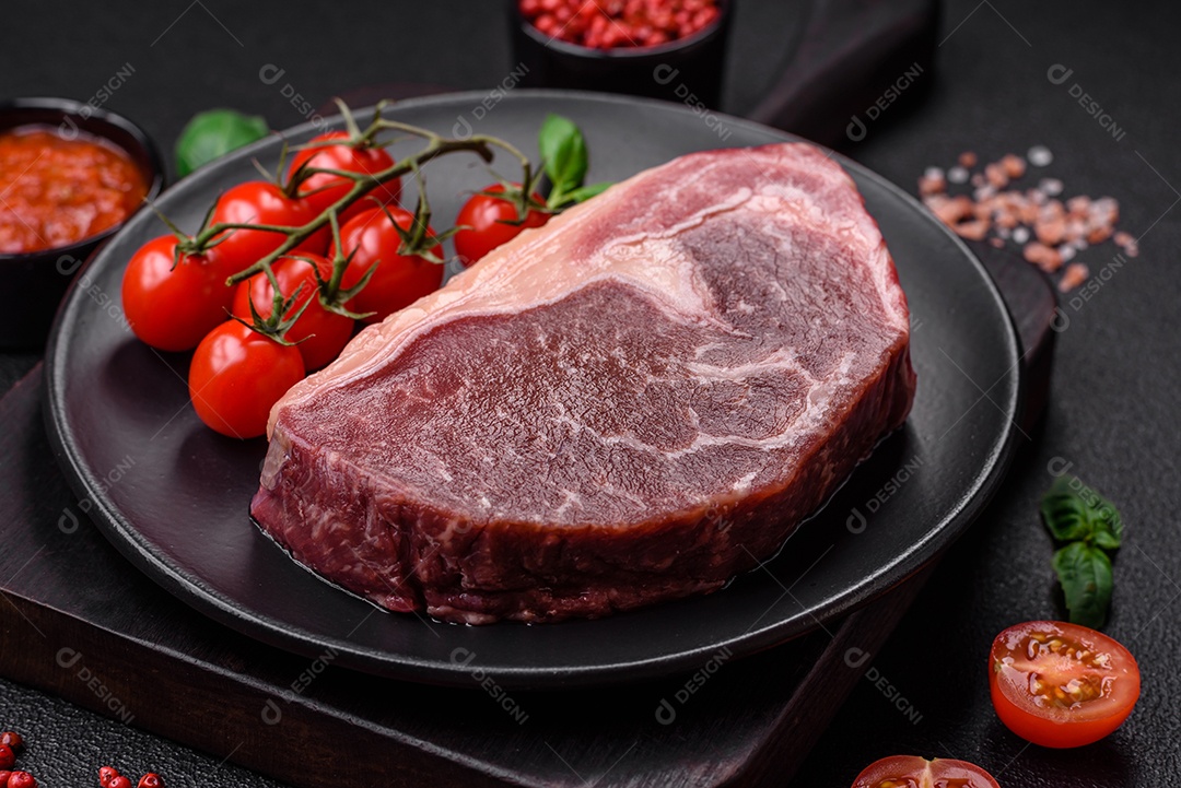 Bife de carne crua fresca com sal, especiarias e ervas sobre um fundo escuro de concreto