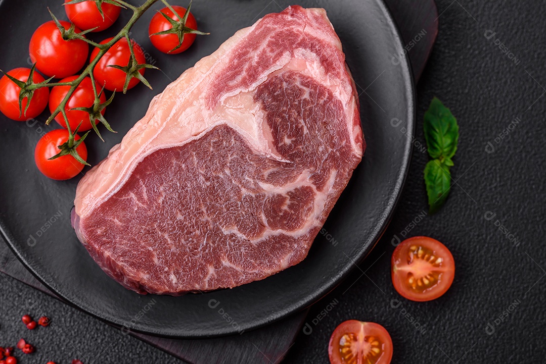 Bife de carne crua fresca com sal, especiarias e ervas sobre um fundo escuro de concreto