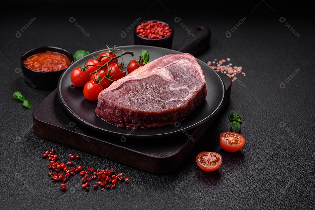Bife de carne crua fresca com sal, especiarias e ervas sobre um fundo escuro de concreto