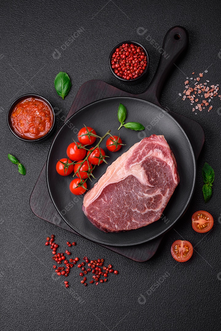 Bife de carne crua fresca com sal, especiarias e ervas sobre um fundo escuro de concreto