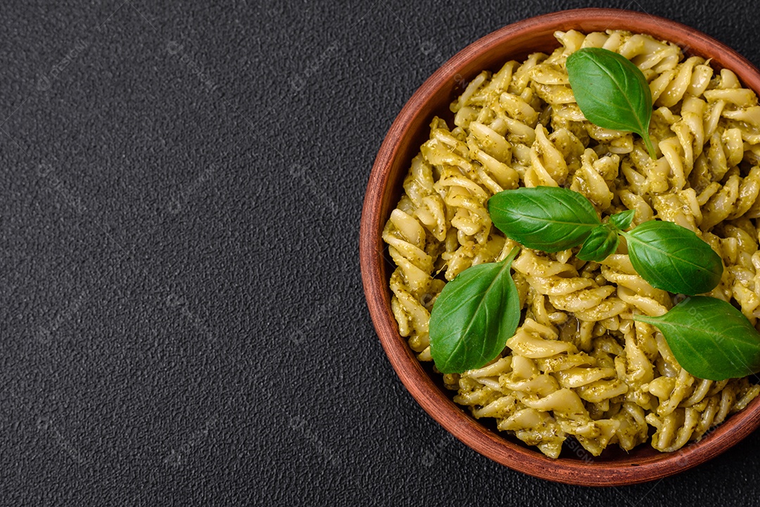 Deliciosa massa fresca com molho pesto verde com manjericão, sal e especiarias sobre fundo escuro de concreto