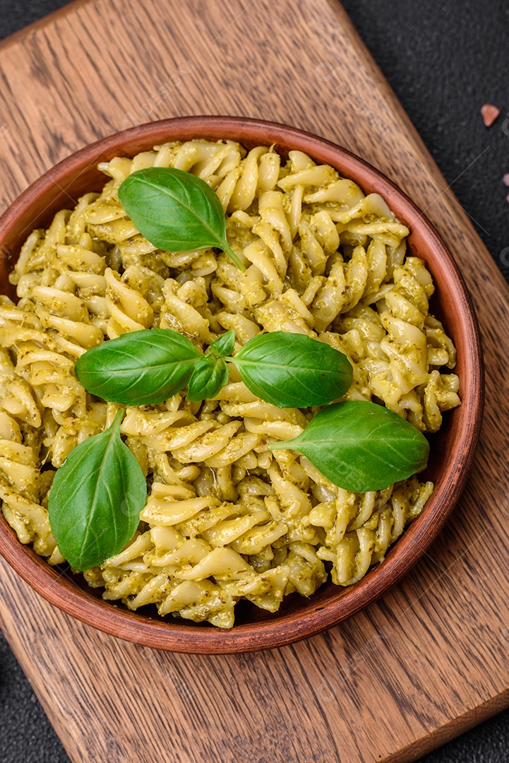 Deliciosa massa fresca com molho pesto verde com manjericão, sal e especiarias sobre fundo escuro de concreto