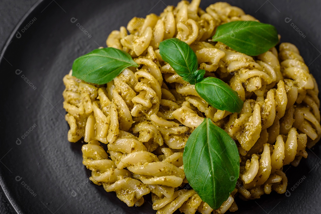 Deliciosa massa fresca com molho pesto verde com manjericão, sal e especiarias sobre fundo escuro de concreto