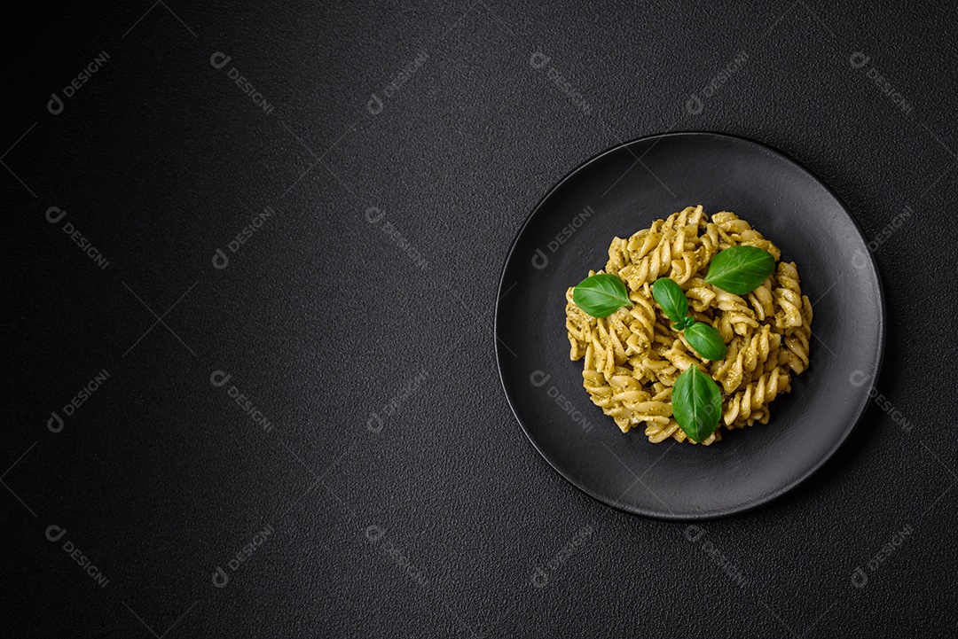 Deliciosa massa fresca com molho pesto verde com manjericão, sal e especiarias sobre fundo escuro de concreto