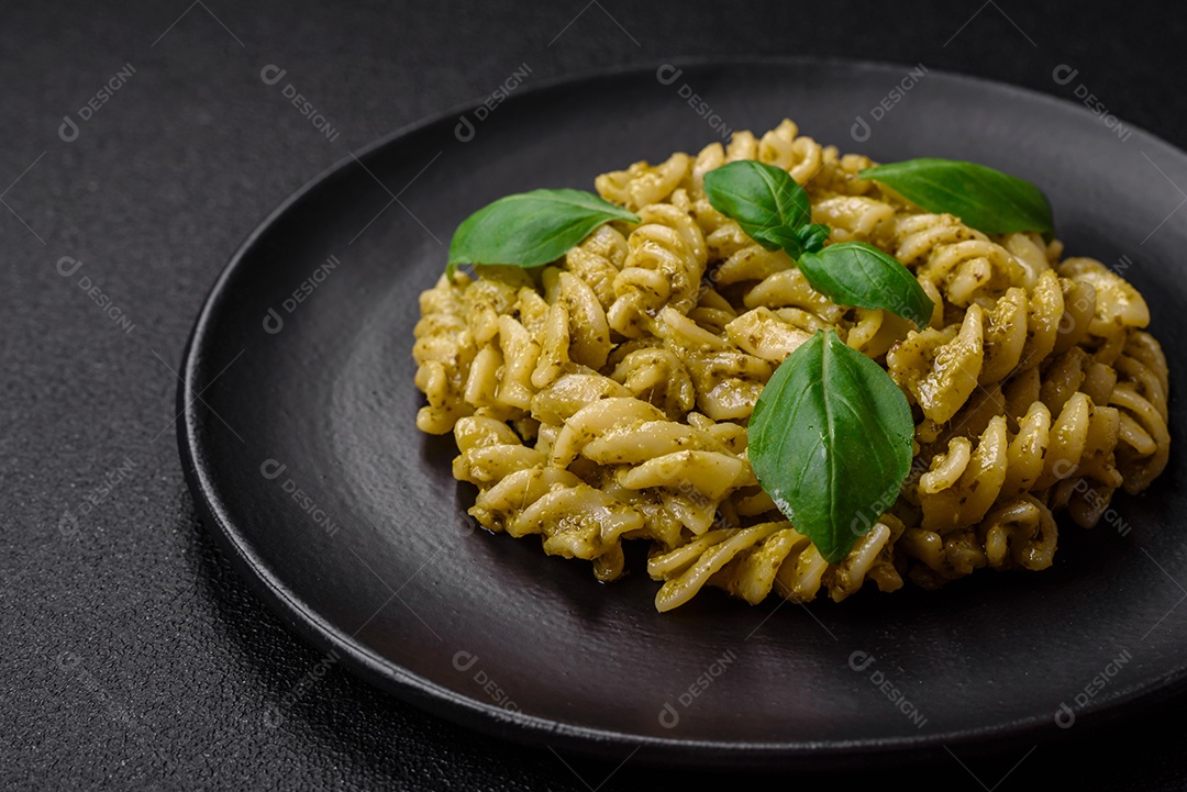 Deliciosa massa fresca com molho pesto verde com manjericão, sal e especiarias sobre fundo escuro de concreto