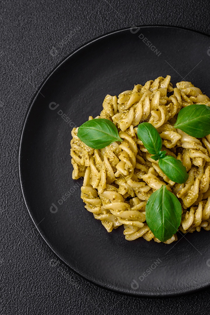 Deliciosa massa fresca com molho pesto verde com manjericão, sal e especiarias sobre fundo escuro de concreto