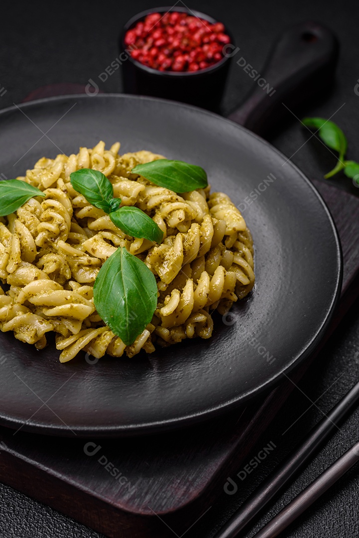 Deliciosa massa fresca com molho pesto verde com manjericão, sal e especiarias sobre fundo escuro de concreto