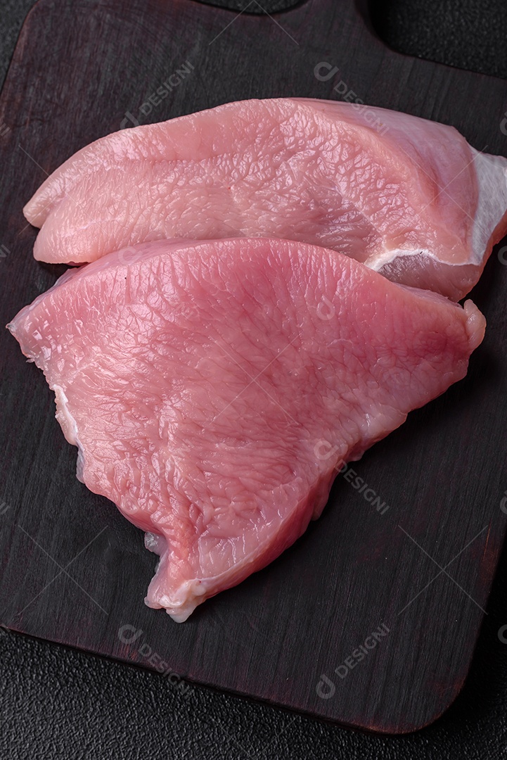 Carne de peru crua em forma de fatias com sal, especiarias e ervas sobre um fundo escuro de concreto