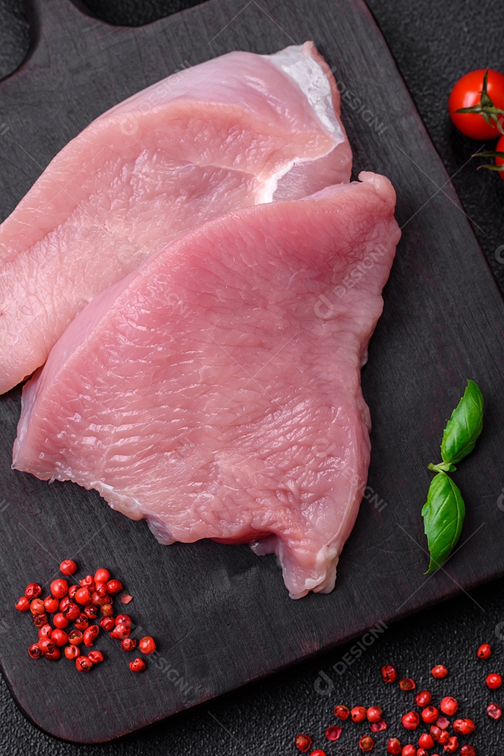 Carne de peru crua em forma de fatias com sal, especiarias e ervas sobre um fundo escuro de concreto