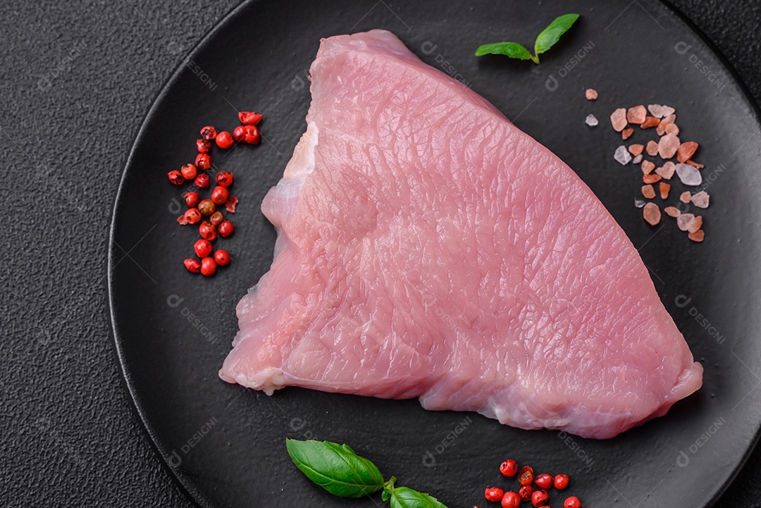 Carne de peru crua em forma de fatias com sal, especiarias e ervas sobre um fundo escuro de concreto