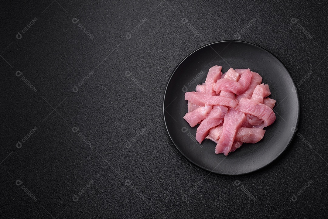 Carne de peru crua em forma de fatias com sal, especiarias e ervas sobre um fundo escuro de concreto