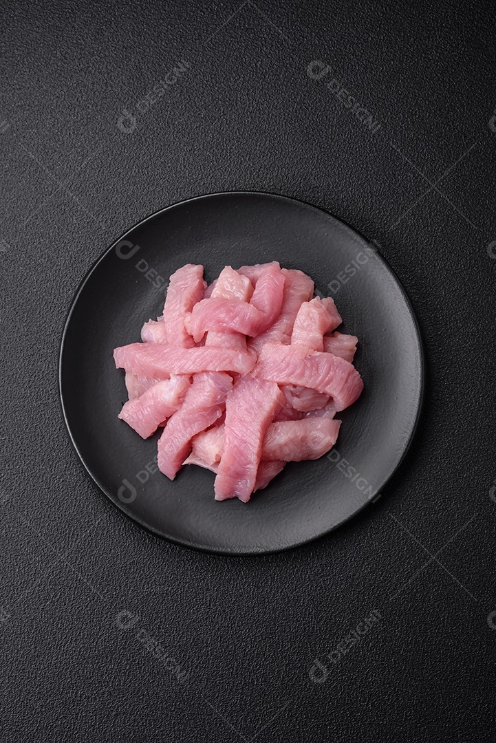 Carne de peru crua em forma de fatias com sal, especiarias e ervas sobre um fundo escuro de concreto