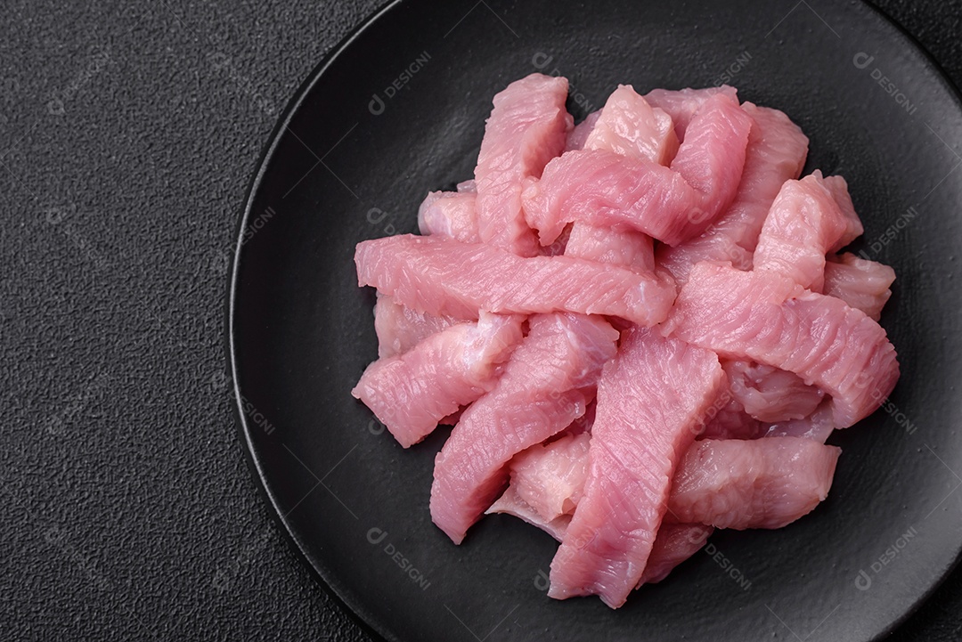 Carne de peru crua em forma de fatias com sal, especiarias e ervas sobre um fundo escuro de concreto