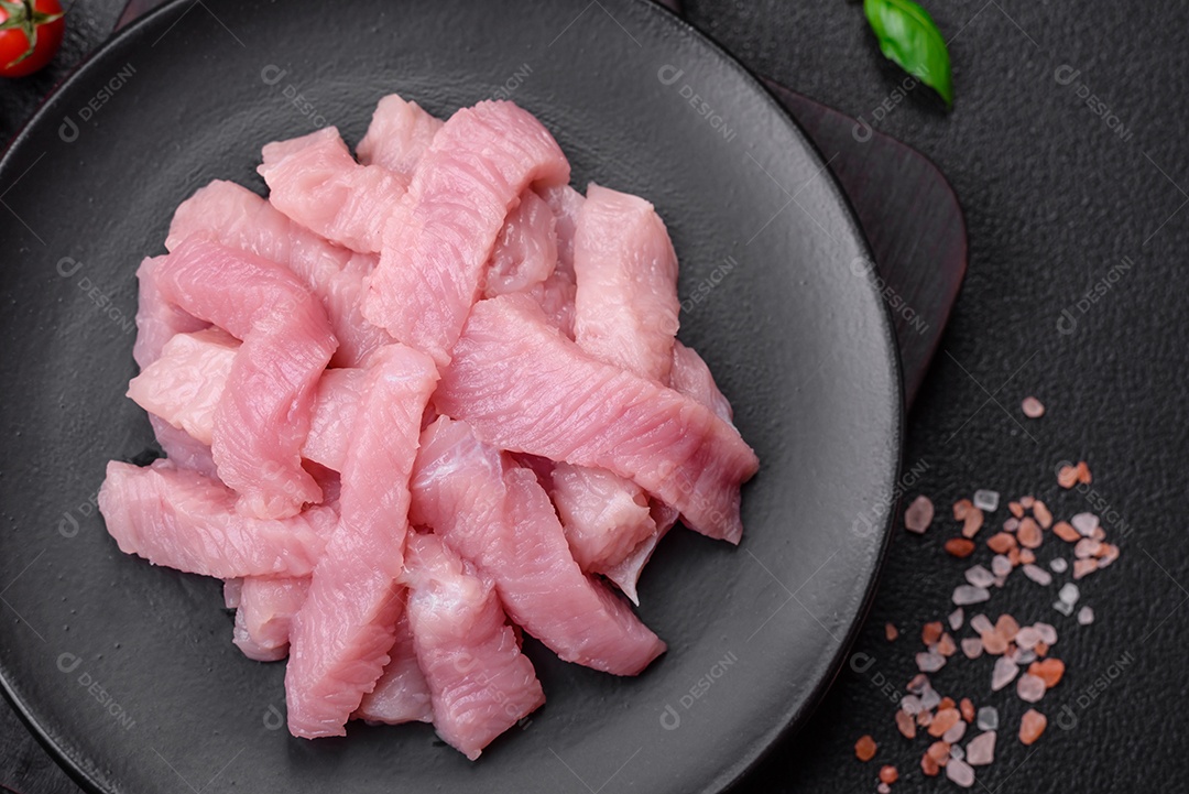 Carne de peru crua em forma de fatias com sal, especiarias e ervas sobre um fundo escuro de concreto