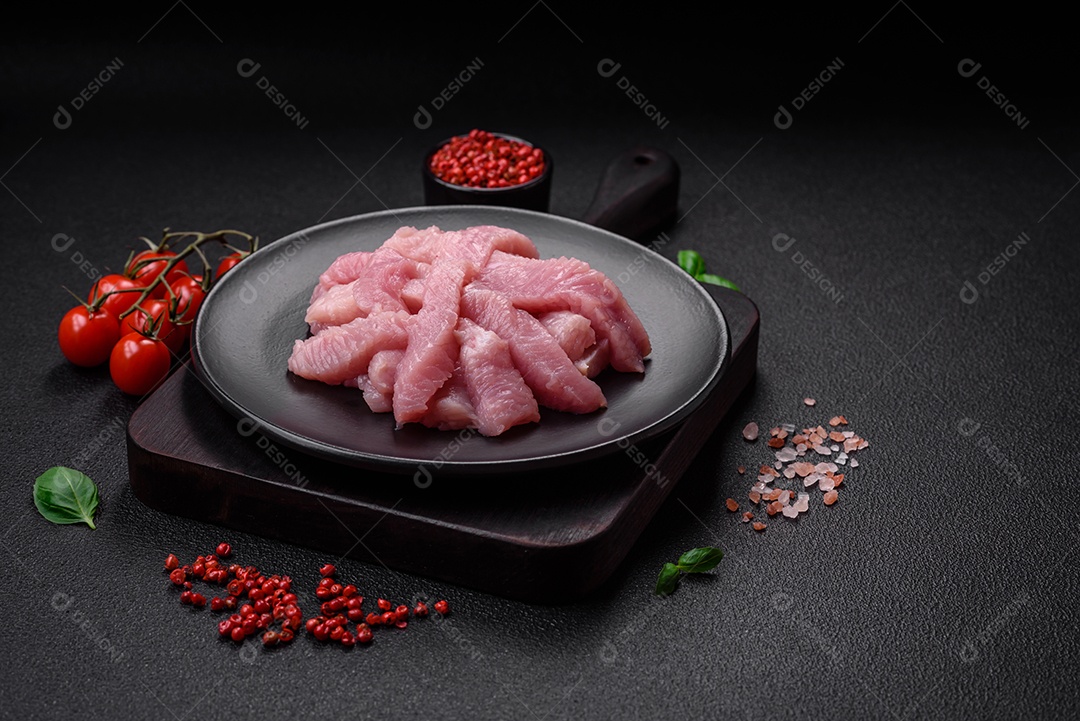 Carne de peru crua em forma de fatias com sal, especiarias e ervas sobre um fundo escuro de concreto