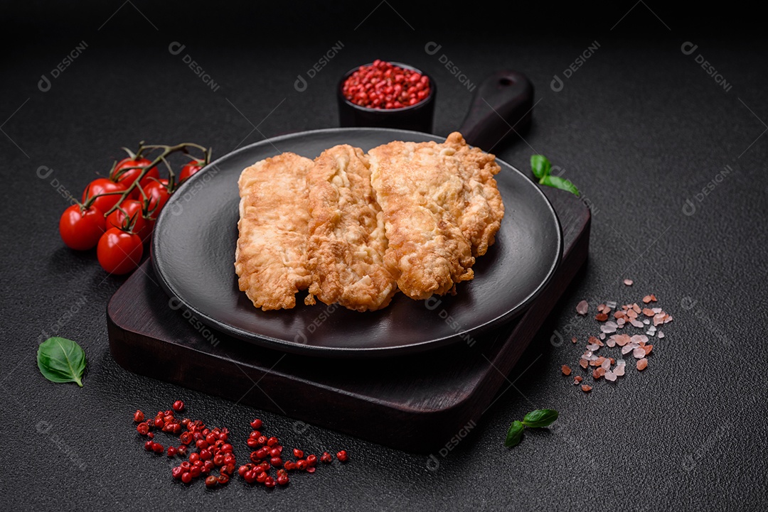 Deliciosa costeleta de frango frito ou carne de porco frita à milanesa com sal, especiarias e ervas sobre um fundo escuro de concreto