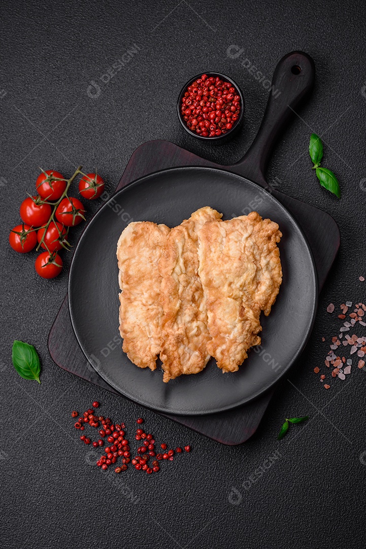 Deliciosa costeleta de frango frito ou carne de porco frita à milanesa com sal, especiarias e ervas sobre um fundo escuro de concreto