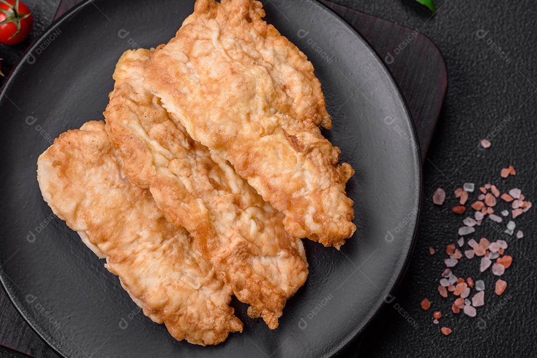 Deliciosa costeleta de frango frito ou carne de porco frita à milanesa com sal, especiarias e ervas sobre um fundo escuro de concreto