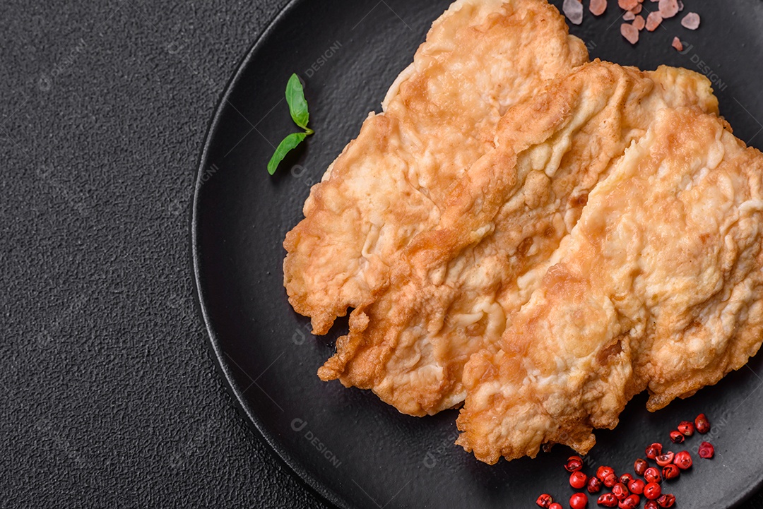 Deliciosa costeleta de frango frito ou carne de porco frita à milanesa com sal, especiarias e ervas sobre um fundo escuro de concreto