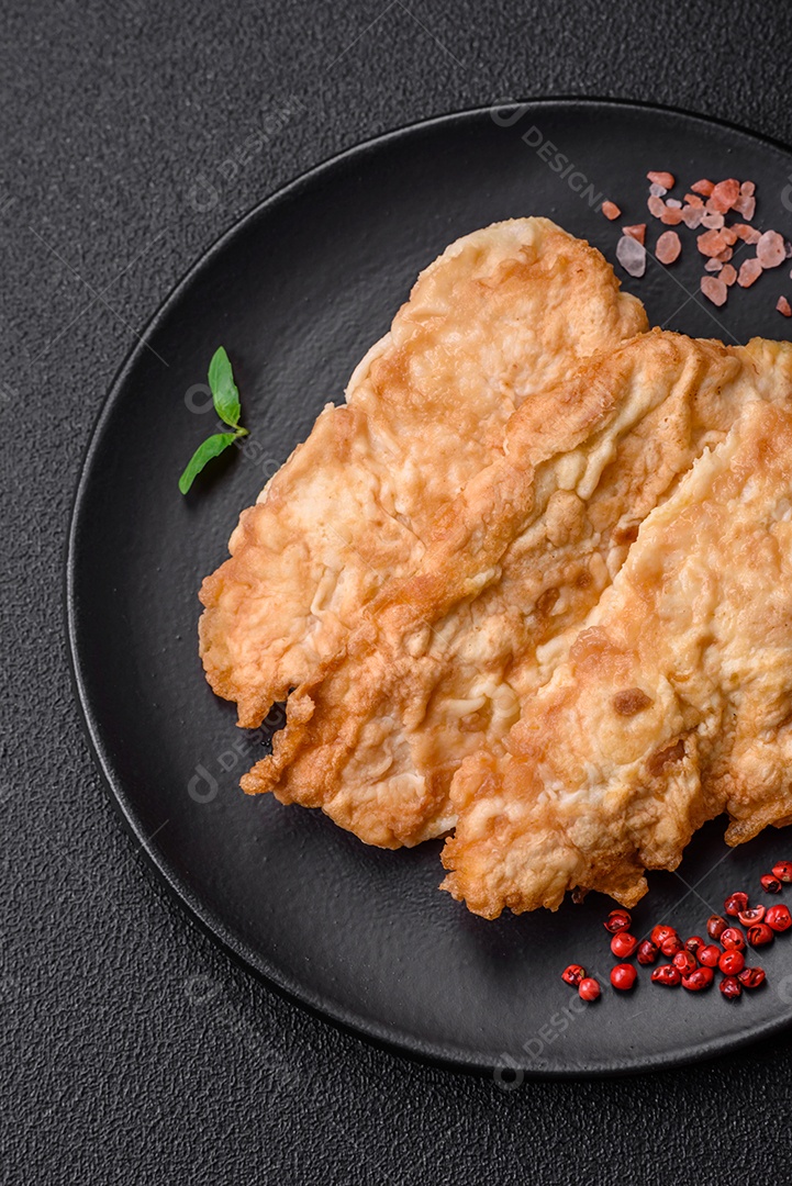 Deliciosa costeleta de frango frito ou carne de porco frita à milanesa com sal, especiarias e ervas sobre um fundo escuro de concreto