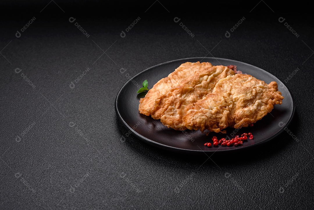 Deliciosa costeleta de frango frito ou carne de porco frita à milanesa com sal, especiarias e ervas sobre um fundo escuro de concreto