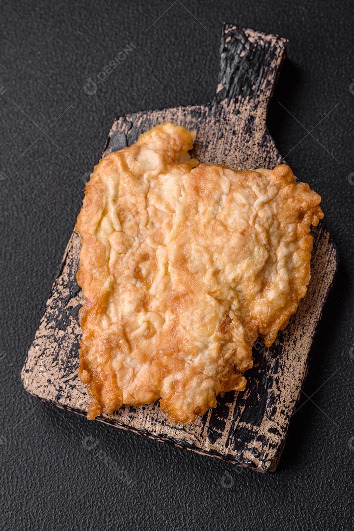 Deliciosa costeleta de frango frito ou carne de porco frita à milanesa com sal, especiarias e ervas sobre um fundo escuro de concreto