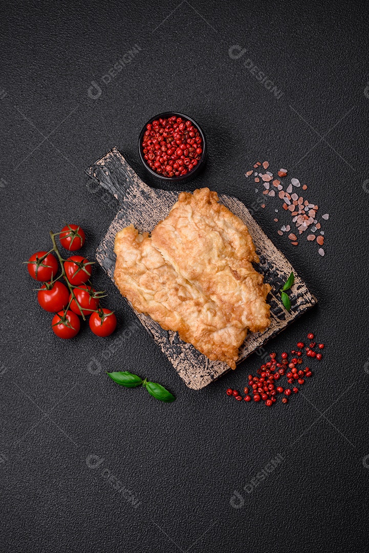Deliciosa costeleta de frango frito ou carne de porco frita à milanesa com sal, especiarias e ervas sobre um fundo escuro de concreto