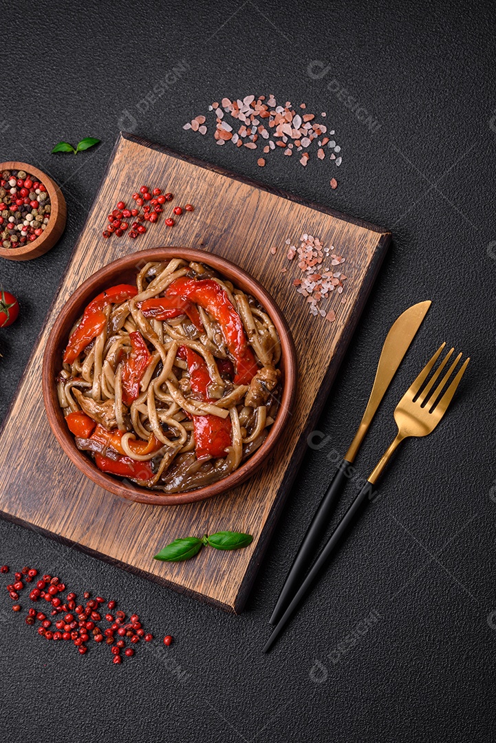 Delicioso prato de udon asiático com legumes, cogumelos, sal e especiarias numa placa cerâmica sobre um fundo escuro de concreto