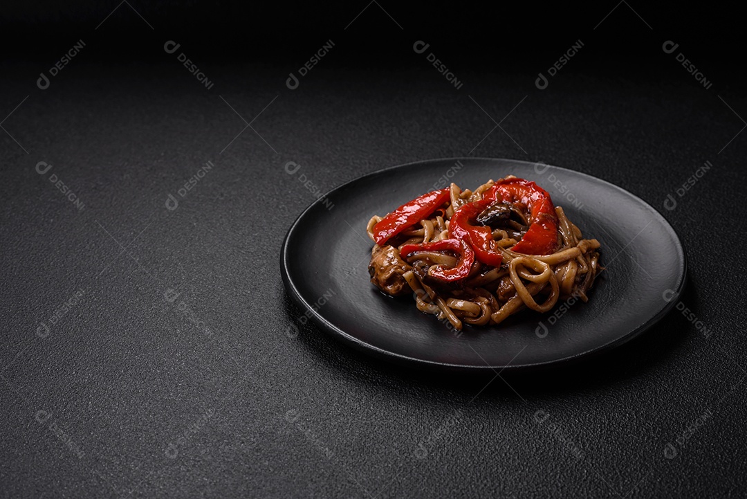 Delicioso prato de udon asiático com legumes, cogumelos, sal e especiarias numa placa cerâmica sobre um fundo escuro de concreto