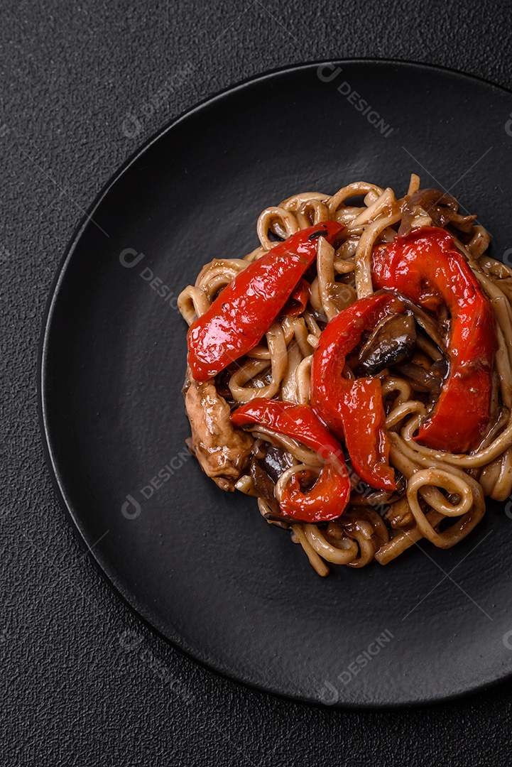 Delicioso prato de udon asiático com legumes, cogumelos, sal e especiarias numa placa cerâmica sobre um fundo escuro de concreto