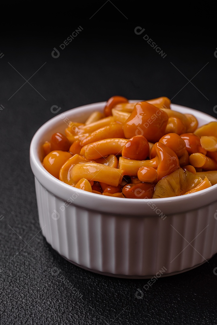 Deliciosos cogumelos em conserva com sal e especiarias em uma placa de cerâmica sobre um fundo escuro e texturizado