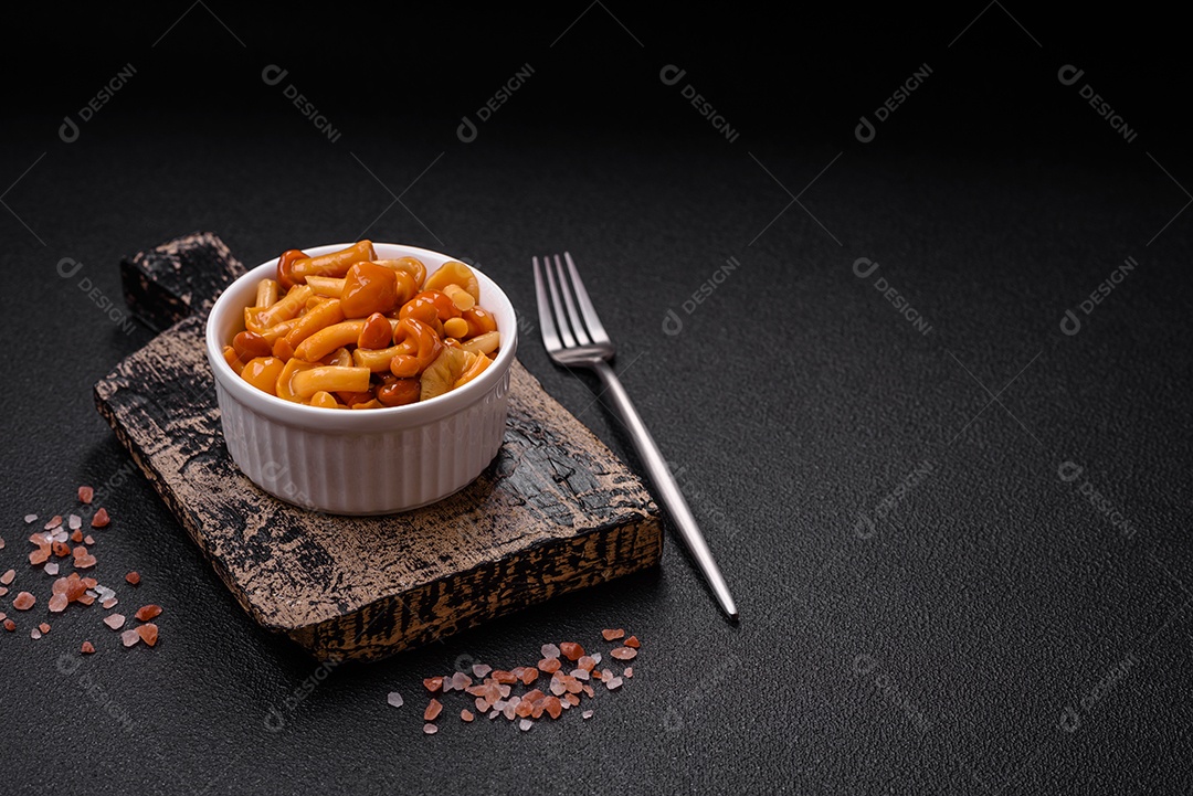 Deliciosos cogumelos em conserva com sal e especiarias em uma placa de cerâmica sobre um fundo escuro e texturizado