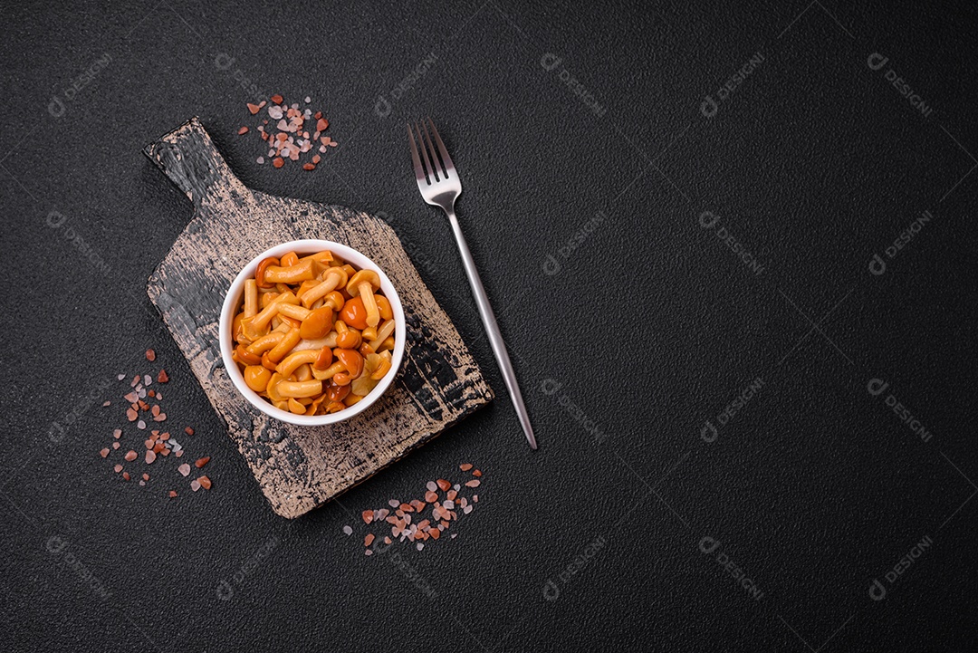 Deliciosos cogumelos em conserva com sal e especiarias em uma placa de cerâmica sobre um fundo escuro e texturizado