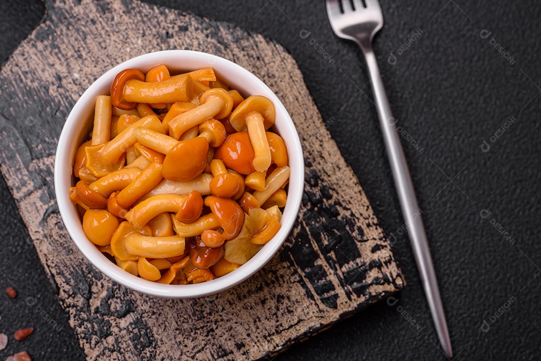 Deliciosos cogumelos em conserva com sal e especiarias em uma placa de cerâmica sobre um fundo escuro e texturizado