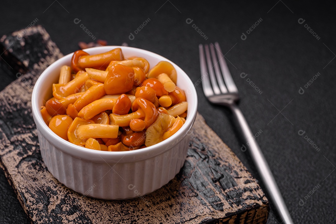 Deliciosos cogumelos em conserva com sal e especiarias em uma placa de cerâmica sobre um fundo escuro e texturizado