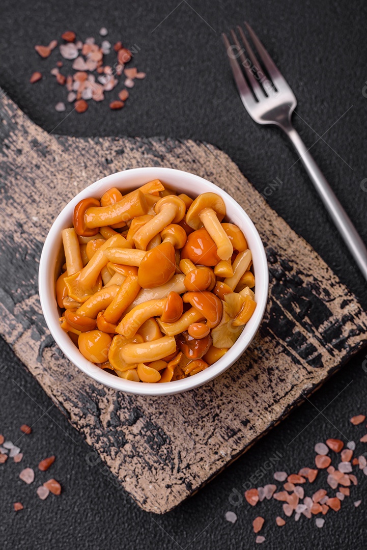 Deliciosos cogumelos em conserva com sal e especiarias em uma placa de cerâmica sobre um fundo escuro e texturizado