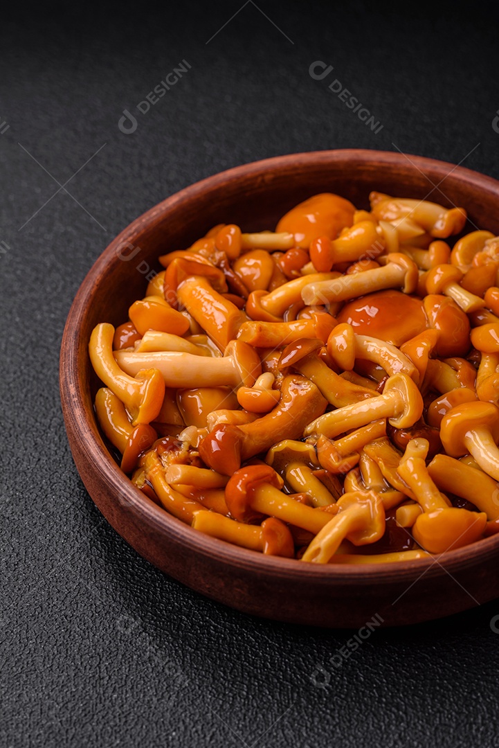 Deliciosos cogumelos em conserva com sal e especiarias em uma placa de cerâmica sobre um fundo escuro e texturizado