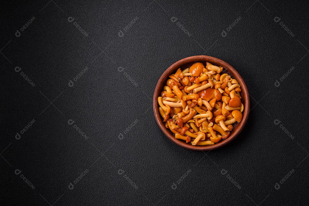 Deliciosos cogumelos em conserva com sal e especiarias em uma placa de cerâmica sobre um fundo escuro e texturizado