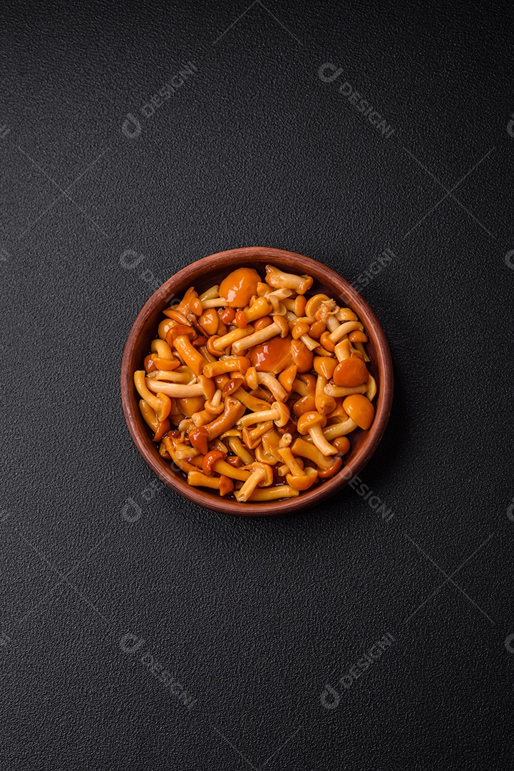 Deliciosos cogumelos em conserva com sal e especiarias em uma placa de cerâmica sobre um fundo escuro e texturizado
