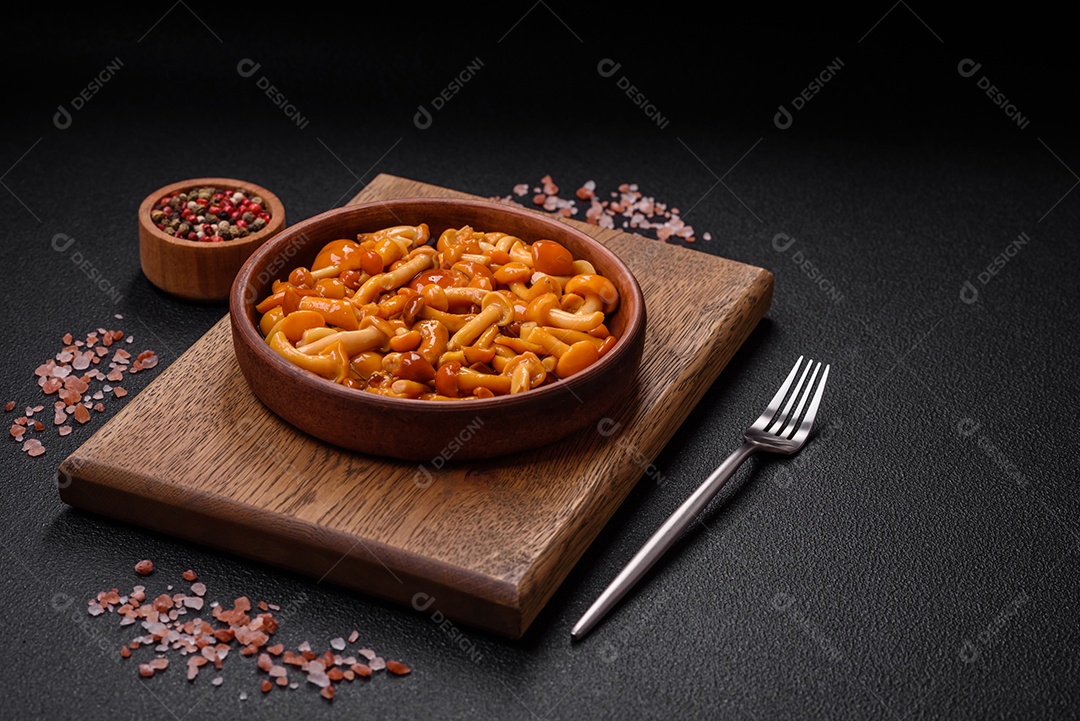 Deliciosos cogumelos em conserva com sal e especiarias em uma placa de cerâmica sobre um fundo escuro e texturizado